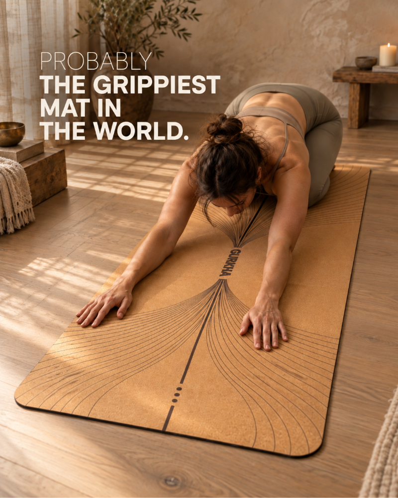 A woman in a yoga pose on a tan textured yoga mat with black curved line graphics and the brand name 'COCOA' printed down the center. The scene is set in a warm, sunlit room with wooden floors and rustic decor, with the text 'PROBABLY THE GRIPPIEST MAT IN THE WORLD.