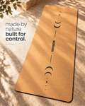 A tan yoga mat with black moon-phase graphics and the brand name 'GURKHA' printed down the center, laid diagonally on a stone surface with dappled sunlight and shadows. Text on the left reads 'made by nature built for control.